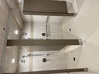 Renovated public shower area with tiled walls, accessible grab bars, and partitioned stalls.