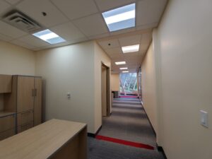 Image of a renovated hallway inside the Civic Centre Resource Library in Vaughan, featuring a wooden desk, modern lighting, red accent flooring, and large windows, upgraded by ICON Restoration.