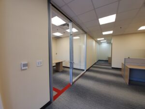 Image of a newly renovated office area at the Vaughan library, featuring a modern wooden desk, overhead cabinet, and updated lighting under a drop ceiling, with a hallway leading to additional workspaces, all part of ICON Restoration's modernization project.