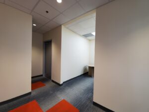 Image of a modern office area at the Vaughan library, featuring a wooden desk with overhead cabinet, updated lighting, and a hallway with red accent flooring, part of ICON Restoration's renovation project.
