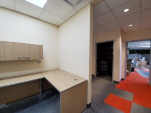 Image of a modern office area at the Vaughan library, featuring a wooden desk with overhead cabinet, updated lighting, and a hallway with red accent flooring, part of ICON Restoration's renovation project.