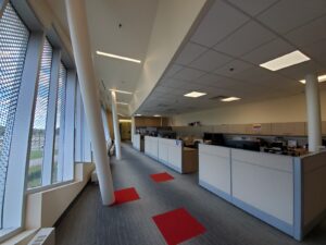 Image of a modernized office corridor at the Vaughan library, featuring updated workstations, large windows with decorative screens, recessed lighting, and red accent flooring, part of ICON Restoration's restoration project.