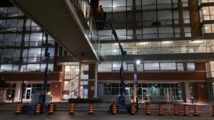 Nighttime maintenance of the pedestrian bridge at Garden City Tower, featuring workers in blue lifts, surrounded by orange safety cones and illuminated buildings, managed by ICON Restoration.