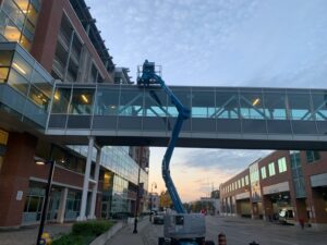 Pedestrian bridge at Garden City Tower under maintenance, with a blue lift and worker accessing the structure, surrounded by urban buildings, managed by ICON Restoration.