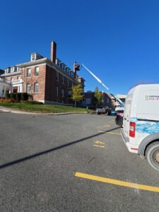 Image of a worker on a lift performing roof repair on a historic brick building at 526 McDonnel Street, Peterborough, ON, with an ICON Restoration van parked nearby under a clear sky.