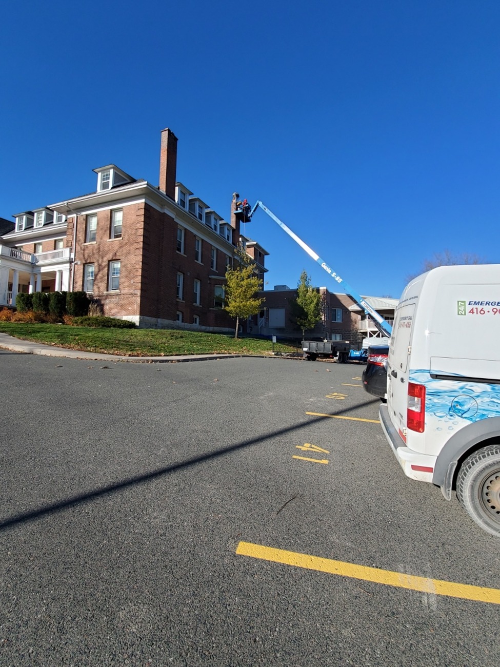 Image of a worker on a lift performing roof repair on a historic brick building at 526 McDonnel Street, Peterborough, ON, with an ICON Restoration van parked nearby under a clear sky.