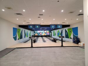A modern bowling alley at Maple Community Centre with polished lanes, vibrant wall art in blue and green, overhead scoreboards, and updated lighting, showcasing the successful restoration by ICON Restoration.