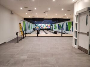 A modern bowling alley with polished lanes, colorful abstract murals in green and purple, new gray tiled flooring, and digital scoring screens, renovated by ICON Restoration at Maple Community Centre.