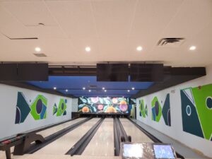 A modern bowling alley at Maple Community Centre with polished lanes, vibrant green and blue geometric wall art, and a colorful digital backdrop, enhanced through restoration by ICON Restoration.