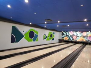 A brightly lit bowling alley at Maple Community Centre with polished lanes, colorful geometric wall art in green and blue, and a vibrant backdrop, showcasing the successful restoration by ICON Restoration.