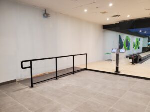 A section of the Maple Community Centre bowling alley featuring newly installed black metal handrails for accessibility, with polished lanes and colorful wall art in the background, restored by ICON Restoration.