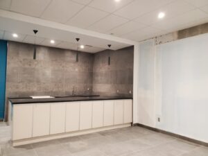 A modern kitchen with a black countertop, white cabinets, gray tiled walls, and pendant lighting, upgraded by ICON Restoration at Maple Community Centre, showcasing a clean and functional space.
