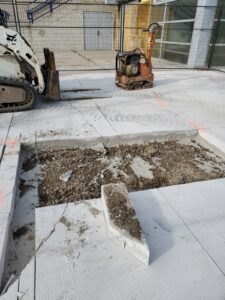Image of the Chancellor Community Centre restoration by ICON Restoration, featuring a construction site with a skid steer loader and compactor, an excavated concrete area, and a fenced-off section under a clear sky in Vaughan.