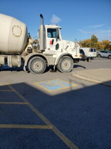 Image of a cement mixer truck from ICON Restoration at the Chancellor Community Centre in Vaughan, parked over an accessible parking space, showcasing ongoing restoration work under a clear blue sky with autumn trees in the background.