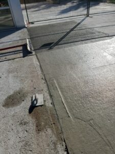 Image of a freshly poured concrete section at the Chancellor Community Centre restoration site in Vaughan, with a trowel and screed tool on the ground, fenced area, and shadows cast under a clear sky, showcasing ICON Restoration's precision work.
