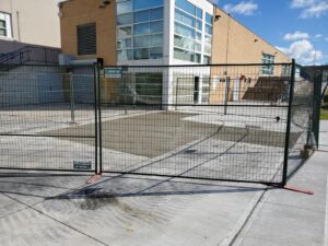 Image of the Chancellor Community Centre restoration by ICON Restoration, featuring a newly expanded concrete area within a fenced-off construction zone, adjacent to a modern building with stairs under a clear sky in Vaughan.