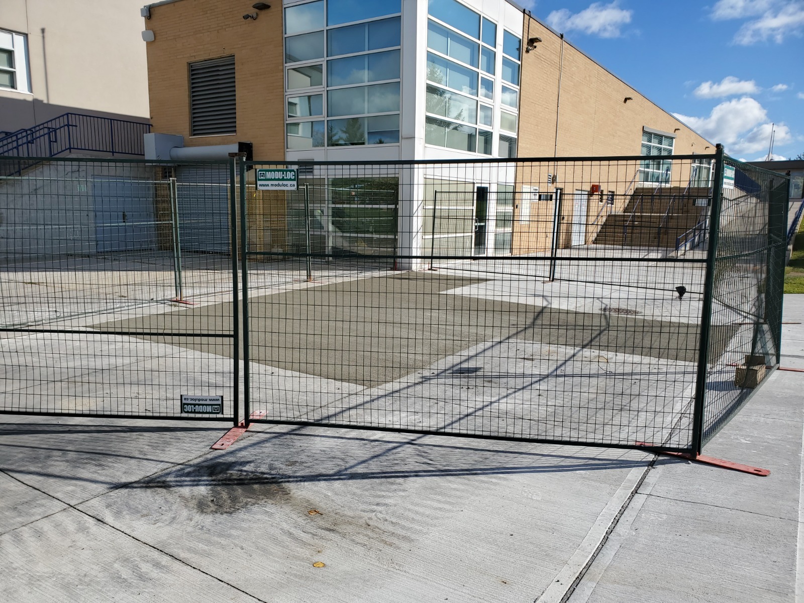 Image of the Chancellor Community Centre restoration by ICON Restoration, featuring a newly expanded concrete area within a fenced-off construction zone, adjacent to a modern building with stairs under a clear sky in Vaughan.
