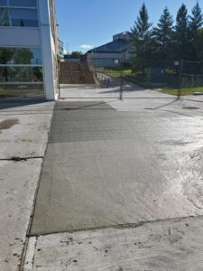 Image of the Chancellor Community Centre restoration by ICON Restoration, featuring freshly poured concrete on the exterior walkway, fenced-off area, and modern building with stairs under a clear blue sky in Vaughan.
