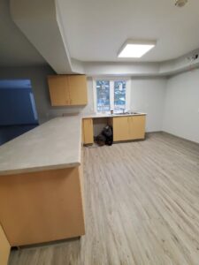 Image of a modern kitchen renovation by ICON Restoration, featuring light wood cabinets, a new countertop, and durable flooring, with large windows allowing natural light, creating a functional and stylish space.
