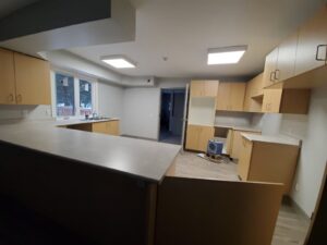 Image of a spacious kitchen renovation by ICON Restoration, featuring light wood cabinets, new countertops, durable flooring, and large windows, with modern lighting and an open layout for a functional space.