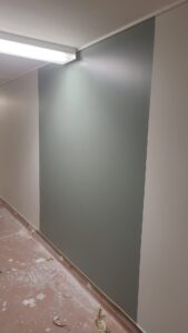A well-lit, modern hallway with polished wooden flooring, gray doors on both sides, an emergency exit sign overhead, and a framed picture on the right wall, showcasing the upgraded interior of 555 Queenston Rd, Cambridge.