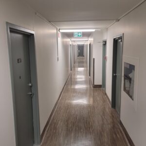 Modern hallway at 555 Queenston Rd, Cambridge, with polished wooden flooring, gray doors labeled 26B, emergency exit signs, and a framed notice, showcasing recent interior renovations.