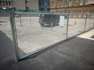 Newly paved parking area at 2 Surrey Place with a drainage channel, construction fence, and a vehicle next to a brick building.