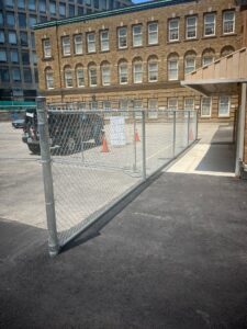 Upgraded parking area at 2 Surrey Place with smooth pavement, drainage channel, construction fence, and a vehicle next to a brick building.