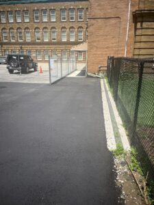 Covered walkway with concrete surface next to a brick building, leading to a fenced-off area with a yellow construction sign at 2 Surrey Place.