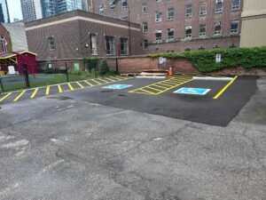 Newly paved parking area at 2 Surrey Place with blue handicap symbols, located near a brick building and a fenced playground.