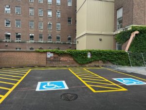Newly paved parking area at 2 Surrey Place with blue handicap symbols, located near a brick building and a fenced playground.