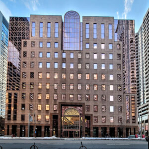Image of a modern multi-story office tower in Toronto with a beige and glass facade, large arched windows, and a snow-lined entrance, surrounded by urban buildings under a partly cloudy sky.