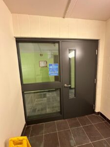 Modern entrance door at Niagara College Canada’s Welland Campus, with a glass panel, black metal frame, and a blue notice sign, upgraded by ICON Restoration.