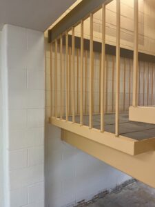Modern staircase at Niagara College Canada’s Welland Campus, showing a newly installed yellow railing and tiled steps against a white brick wall, post-restoration by ICON Restoration.