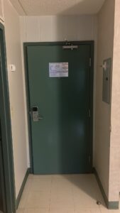 Modern emergency exit door at Niagara College Canada’s Welland Campus, with a green door, electronic lock, and safety notice, upgraded by ICON Restoration.