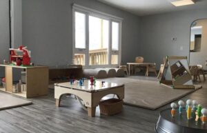 Image of the renovated interior of the RAA-1815 Minden Daycare Centre by ICON Restoration, featuring a modern room with gray walls, large windows, durable flooring, child-sized tables, chairs, and educational toys, creating a safe and engaging environment.
