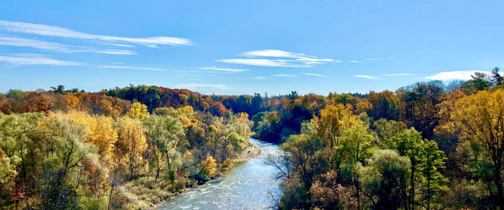 A scenic view of a river winding through a valley filled with trees in vibrant autumn colors under a clear blue sky.