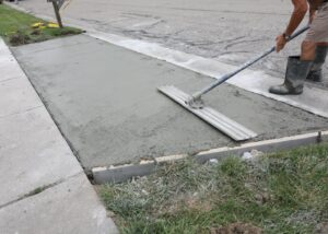 A worker leveling fresh concrete on a walkway with a screed.