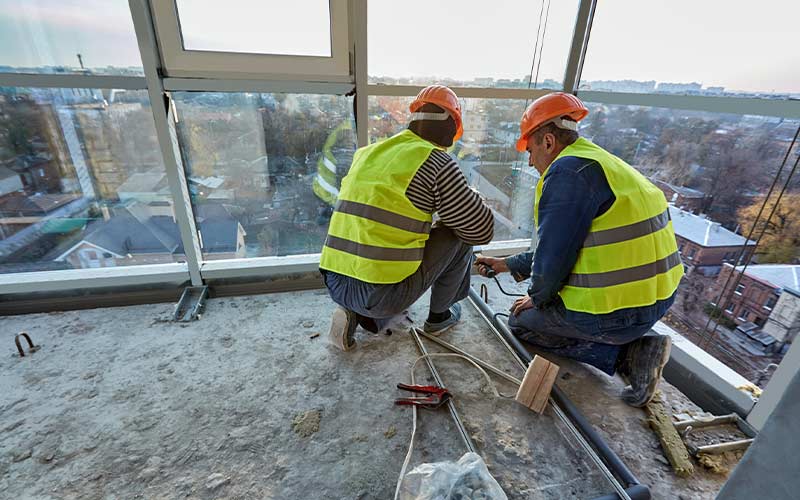 Two workers in safety vests and helmets installing a balcony with glass railings.