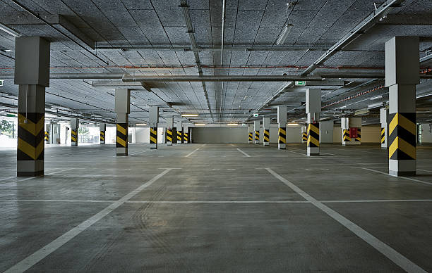 A wide parking garage with concrete pillars, yellow-black barriers, and overhead lighting.